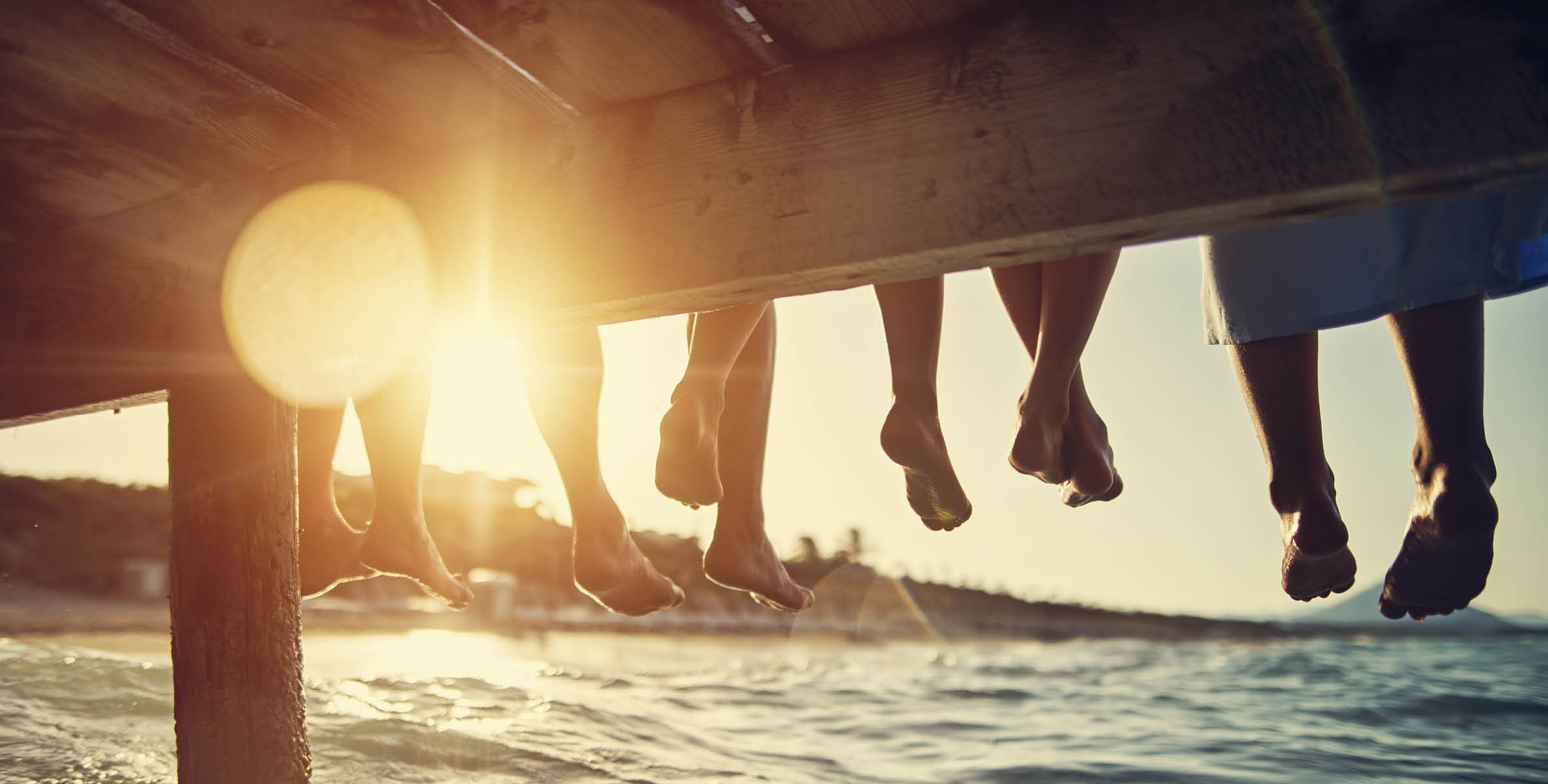 Five people having fun sitting on pier. Feet shot from below the pier. Sunny summer day evening. Nikon D850