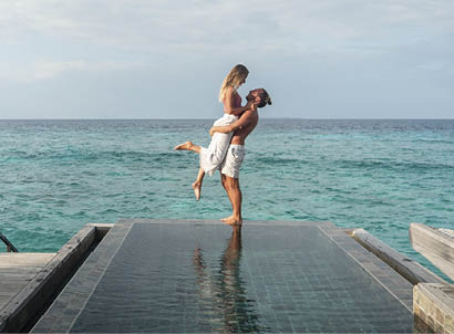 Couple enjoying tropical vacations from the edge of an infinity pool in private over water villa. People travel luxury holidays