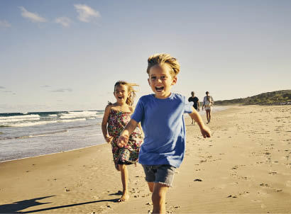 Shot of two adorable little children running at the beach with their parents in the background