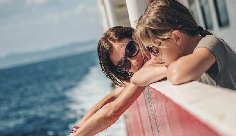 Mother and daughter traveling on a ferry boat and standing on a ship deck on a sunny day