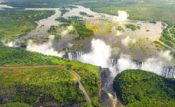 Victoria Falls in Zimbabwe and Zambia, Aerial helicopter photo, green forest around amazing majestic waterfalls of Africa  Livingston Bridge above the river