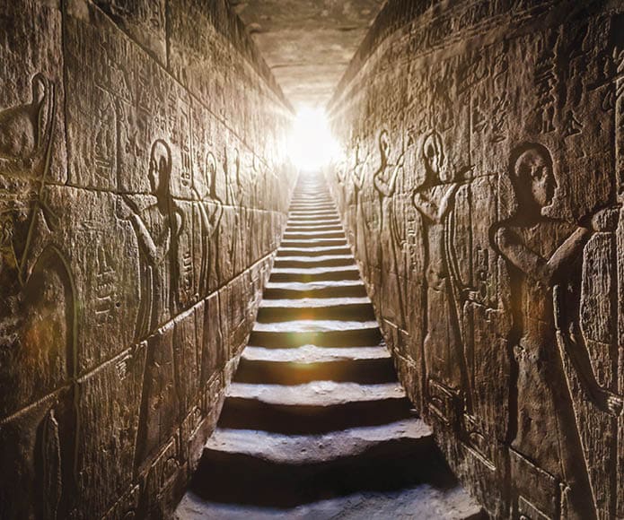 Temple of Edfu, Egypt  Passage flanked by two glowing walls full of Egyptian hieroglyphs, illuminated by a warm orange backlight from a door at the end of the stairs 