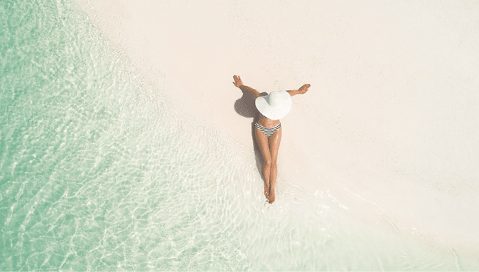 Summer holiday fashion concept - tanning girl wearing sun hat at the beach on a white sand shot from above Top view from drone  Aerial view of slim woman sunbathing lying on a beach in Maldives 