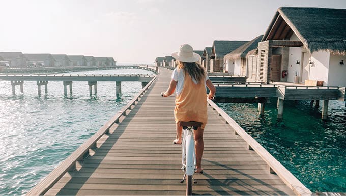 Tropical vacations, young woman with bicycle on wooden pier in the Maldives  Female enjoying bike ride on jetty over coral reef water  Dreamlike destination