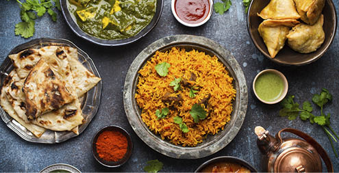 Top view of Indian traditional dishes and appetizers: chicken curry, pilaf, naan bread, samosas, paneer, chutney on rustic background. Table with choice of food of Indian cuisine, dinner/buffet