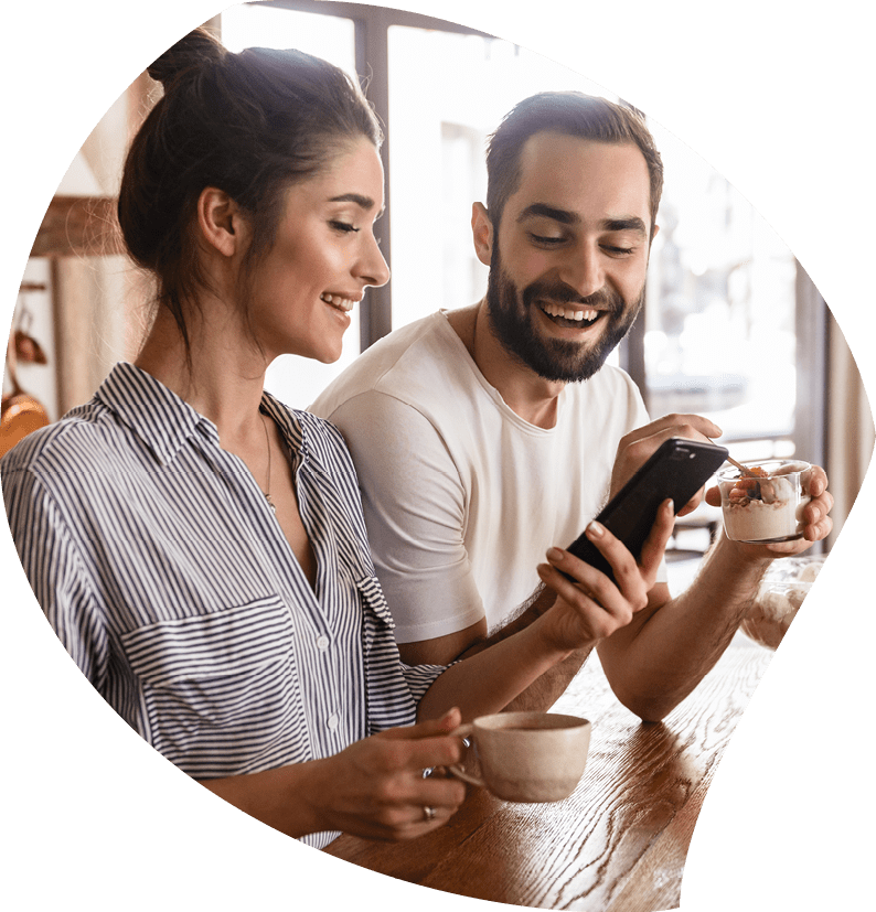 Photo of european brunette couple man and woman 20s drinking coffee and using cell phone during breakfast in kitchen at home