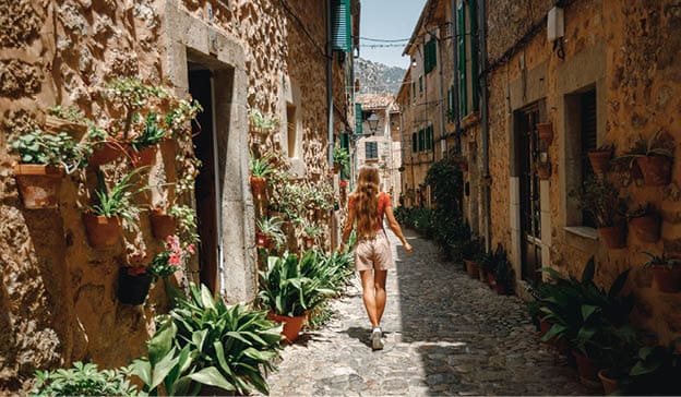 Back view young girl tourist walk through cozy and beautiful  street decorated with flower pots and ceramic tiles in Valldemossa, Mallorca, Spain  Vacation in Spain