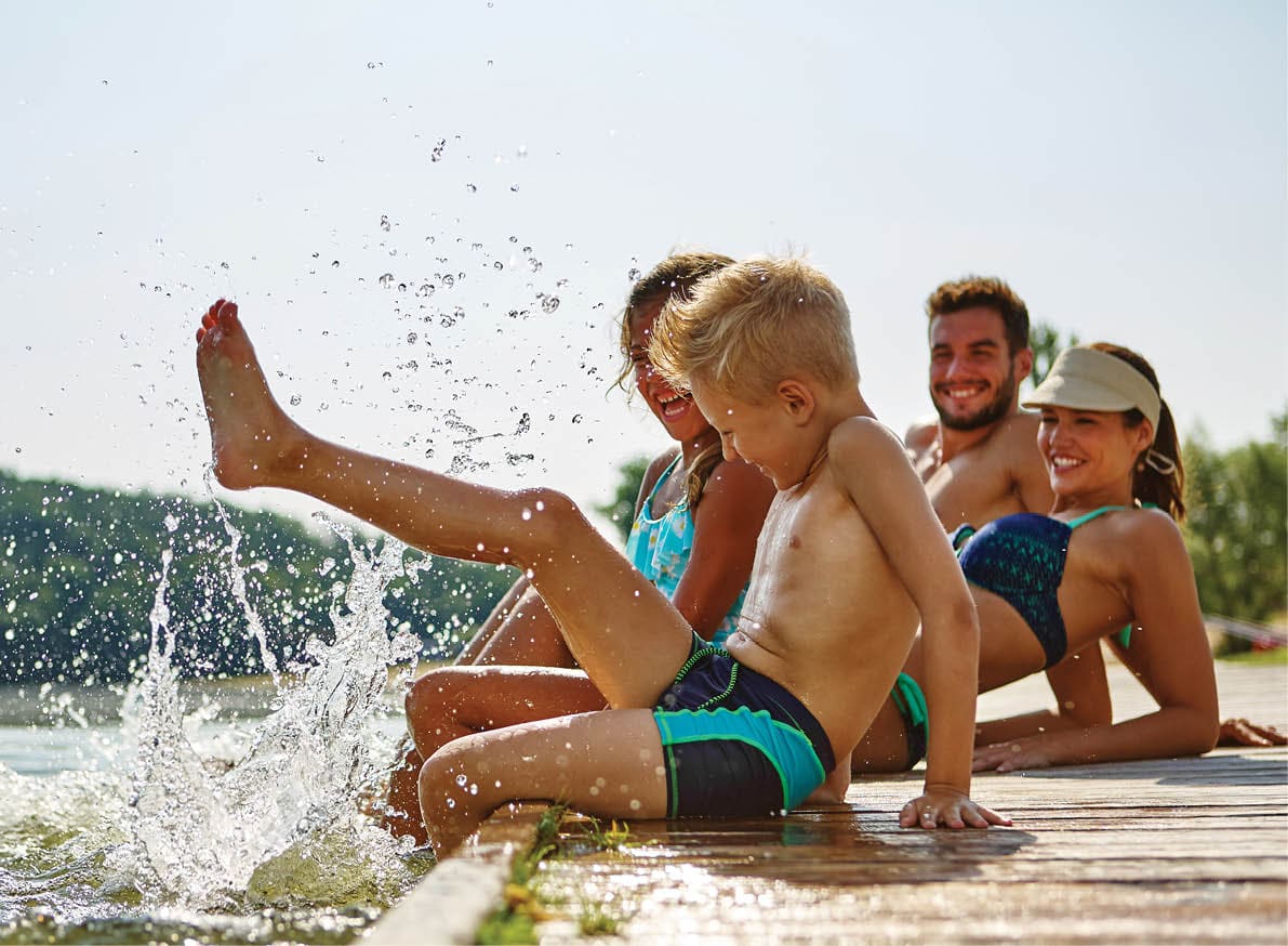 Familie am See badet glücklich mit Füßen im Wasser im Sommer
