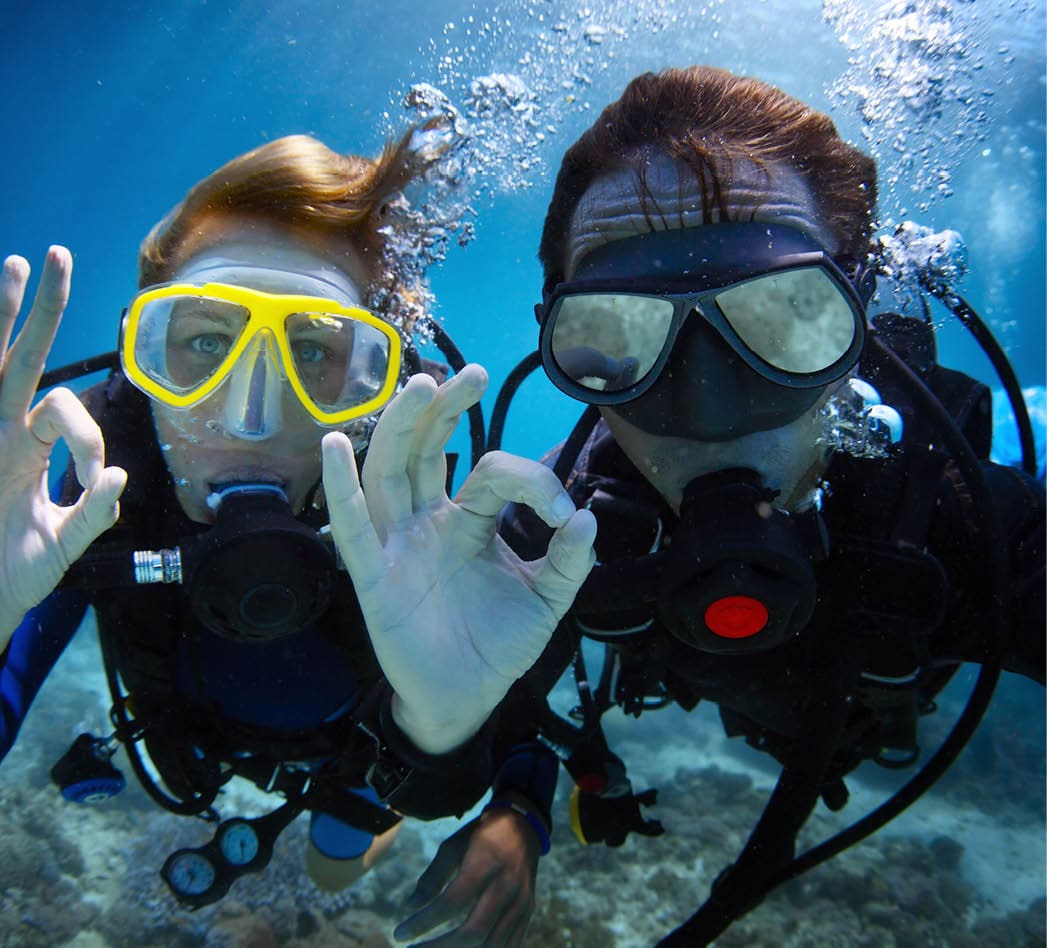 Underwater shoot of a young couple diving with scuba in a tropical sea and showing ok signal