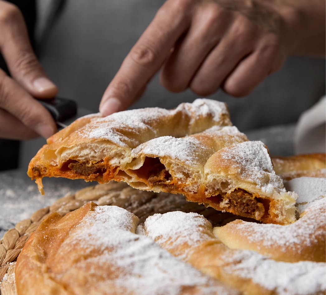 closeup of a young caucasian man serving a piece of on an ensaimada, a pastry typical of Mallorca, Spain, filled with sobrasada, placed on a rustic wooden table