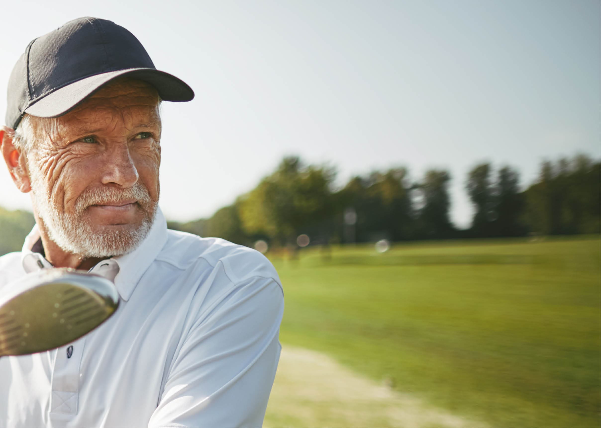 Smiling senior man standing by a golf cart looking out at the fairway while playing a round of golf on a sunny day