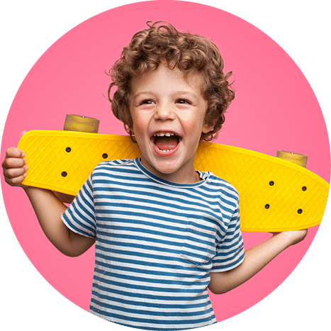 Happy curly boy laughing and holding bright colored skateboard over vibrant pink background isolated