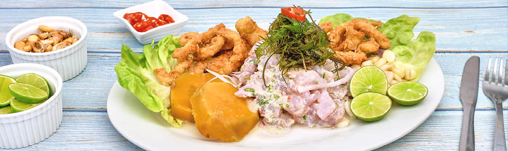 Peruvian food: fish ceviche and chicharron de pescado with fried cassava, sweet corn and sweet potato, served on a white plate, Traditional Peruvian ceviche accompanied by fish, corn pancake, sweet potato, canchita and plenty of spicy juice  Ceviche y chicharron de pescado
