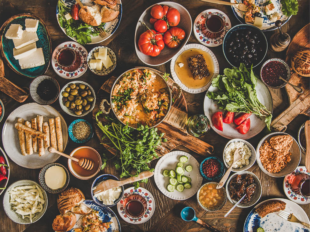 Turkish breakfast table  Flat-lay of fresh pastries, vegetables, greens, olives, cheeses, fried eggs, jams, honey, tea in copper pot and tulip glasses, top view  Middle Eastern meal