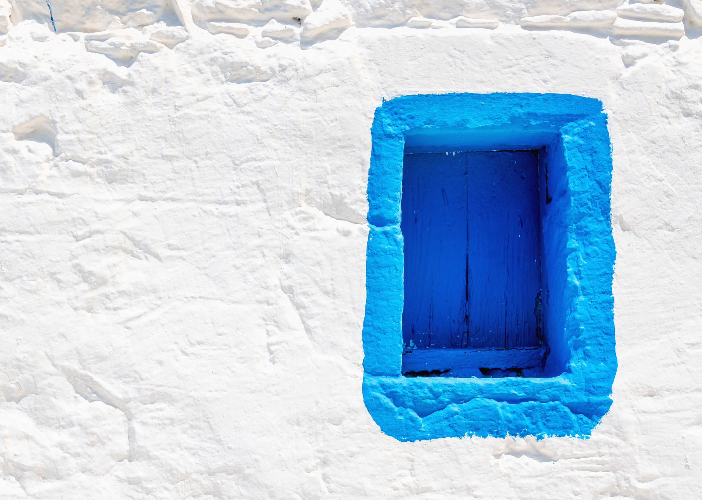 Iconic blue wooden window on white stone wall of typical Greek house, Greece