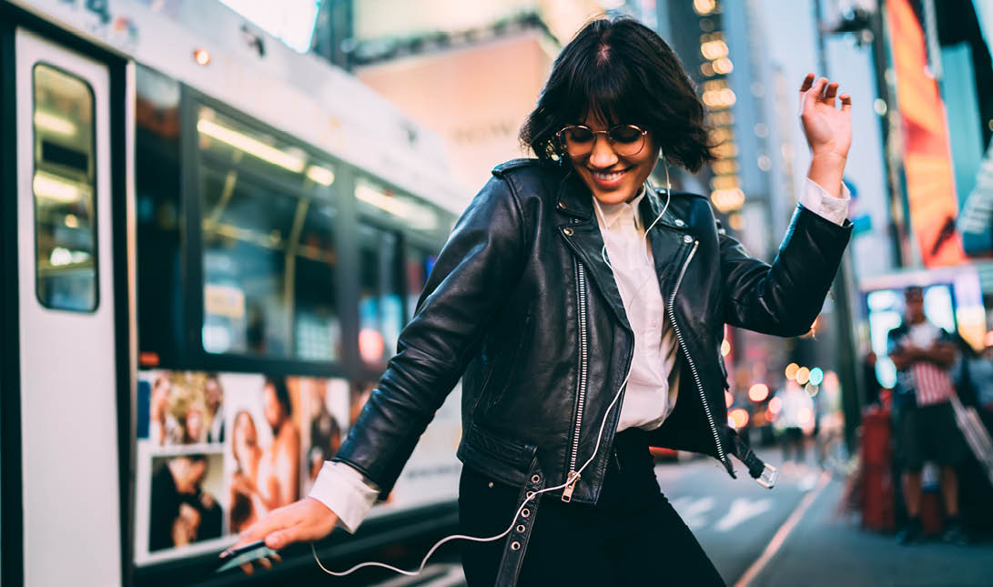 Carefree woman in fashionable clothing listening funny audio and dancing during evening walk in New York City, cheerful female enjoying adolescent music podcast during nightlife lifestyle in Manhattan