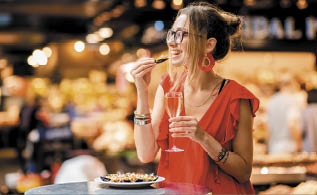 Young woman in red dress having lunch with mussels and rose wine sitting at the food market