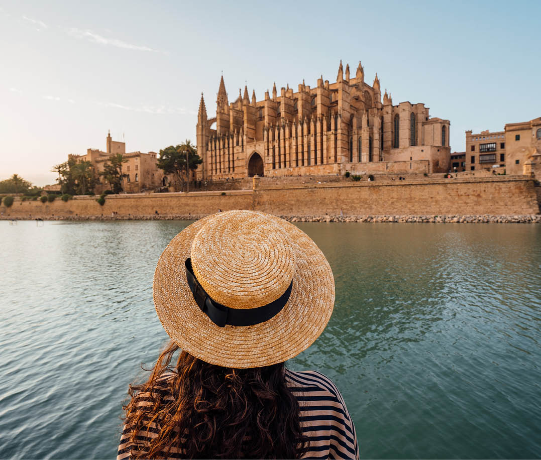 Rear view of a woman with a straw hat while she's admiring the Cathedral de Santa Mar a de Palma de Mallorca at sunset. The Cathedral reflects in the water.