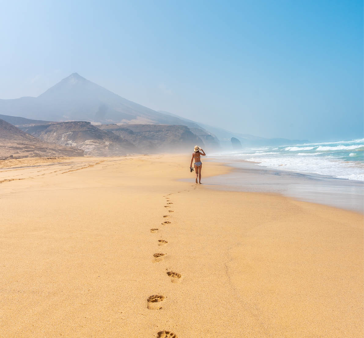 A young tourist walking alone on the wild beach Cofete in the natural park of Jandia, Barlovento coast, south of Fuerteventura, Canary Islands. Spain