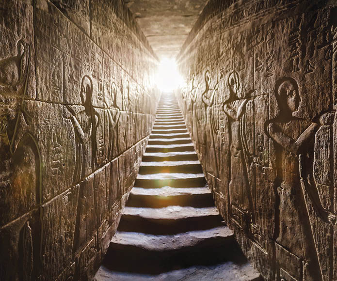 Temple of Edfu, Egypt. Passage flanked by two glowing walls full of Egyptian hieroglyphs, illuminated by a warm orange backlight from a door at the end of the stairs.