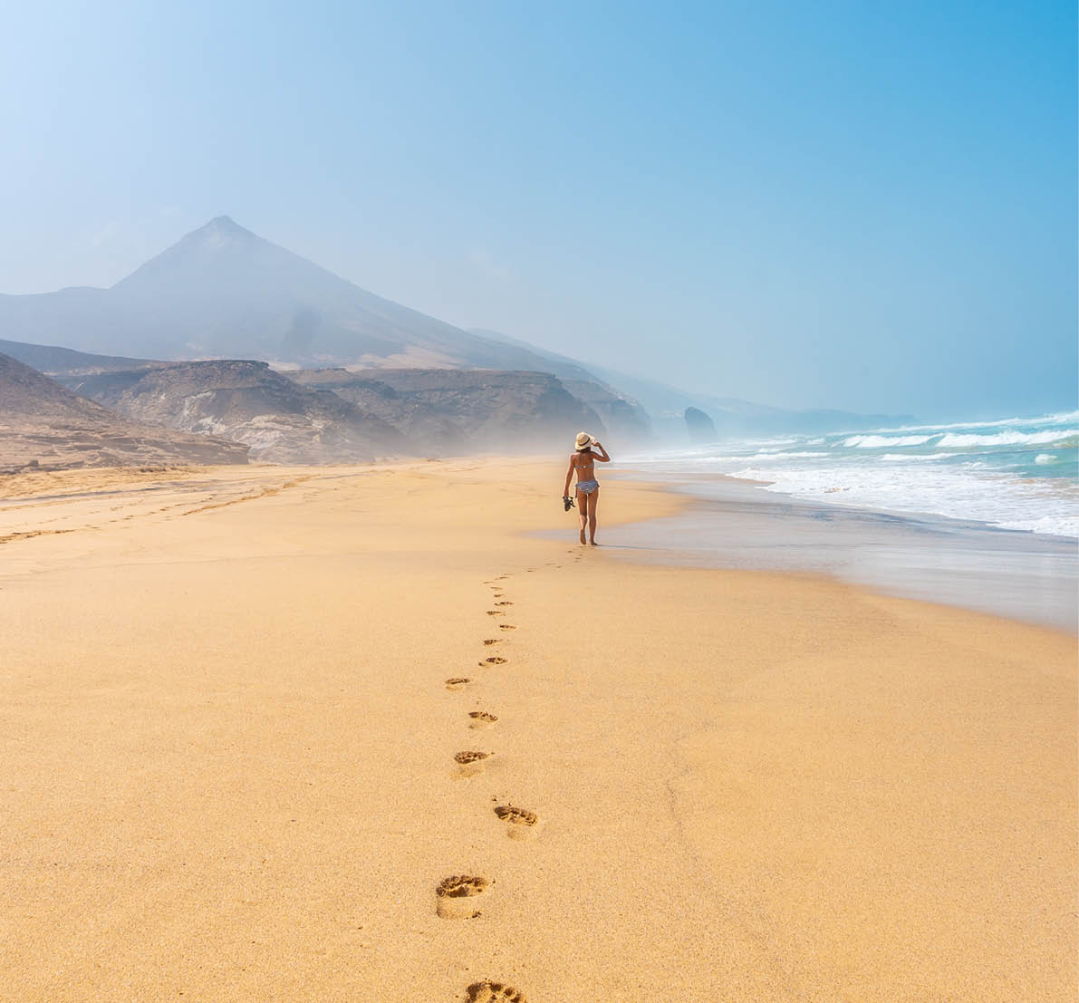 A young tourist walking alone on the wild beach Cofete in the natural park of Jandia, Barlovento coast, south of Fuerteventura, Canary Islands. Spain