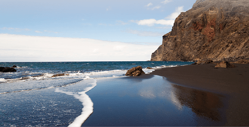 A black sand beach at the atlantic ocean at La Gomera, one of the canary islands. The sky is morrored in the wet sand.