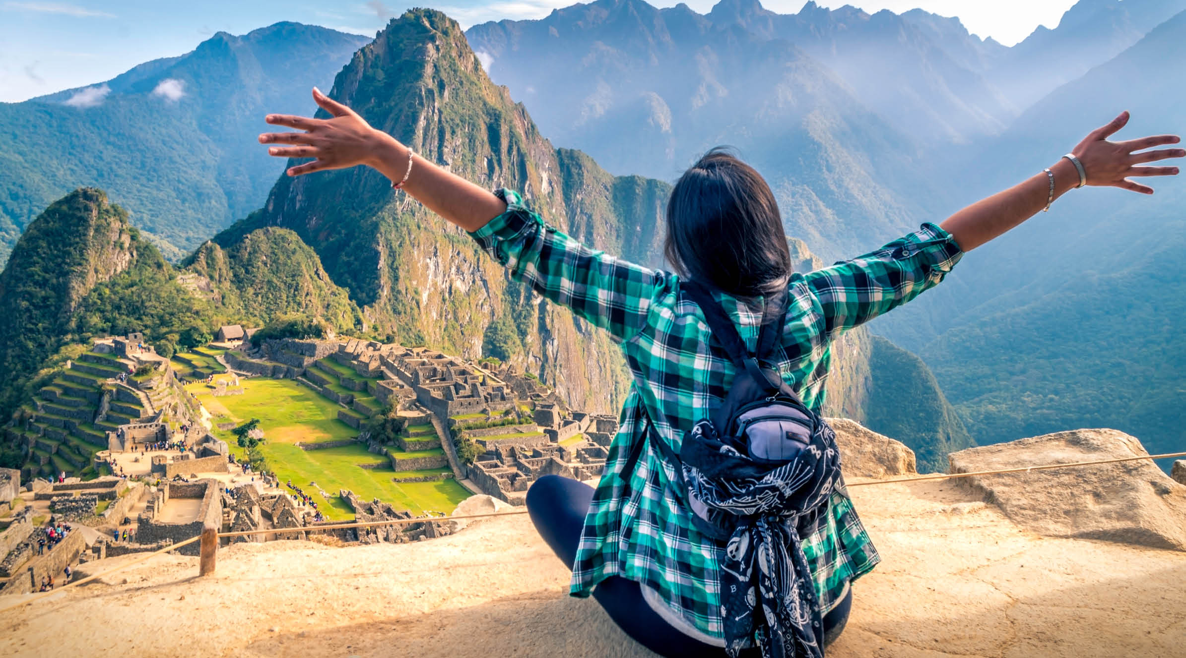A woman tourist contemplating the amazing landscape of Machu Picchu with arms open. Archaeological site, UNESCO World Heritage
