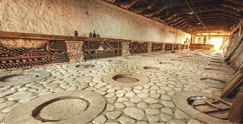 Huge stone cellar with aged dust wine bottles and qvevri, large earthenware vessels under ground. Rustic farmhouse interior with rural storage of winery
