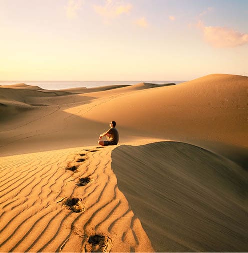 Man sitting and relaxing on sand dunes by the sunrise, in Maspalomas on Gran Canaria 