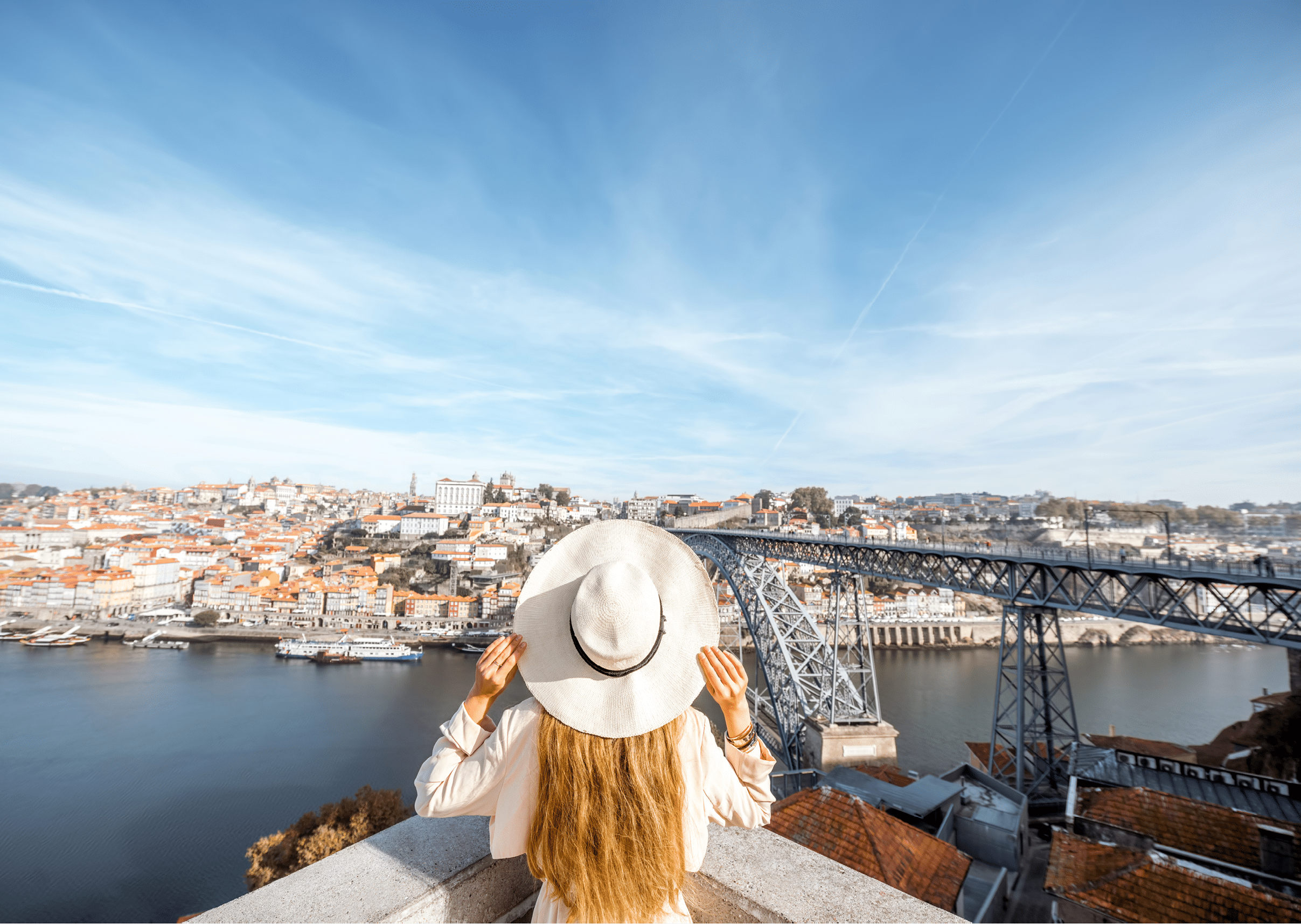 Young woman traveler in sunhat standing back on the beautiful aerial cityscape background with Douro river and Luise bridge during the morning light in Porto, Portugal