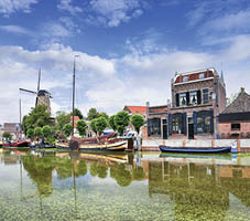 Smooth green canal with moored boats and monumental houses in the old town of Gouda, The Netherlands 