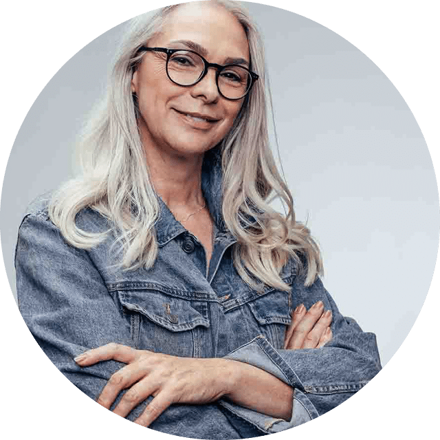 Beautiful mature caucasian female with eyeglasses looking at camera and smiling  Senior woman in casuals standing with her arms crossed against grey background 