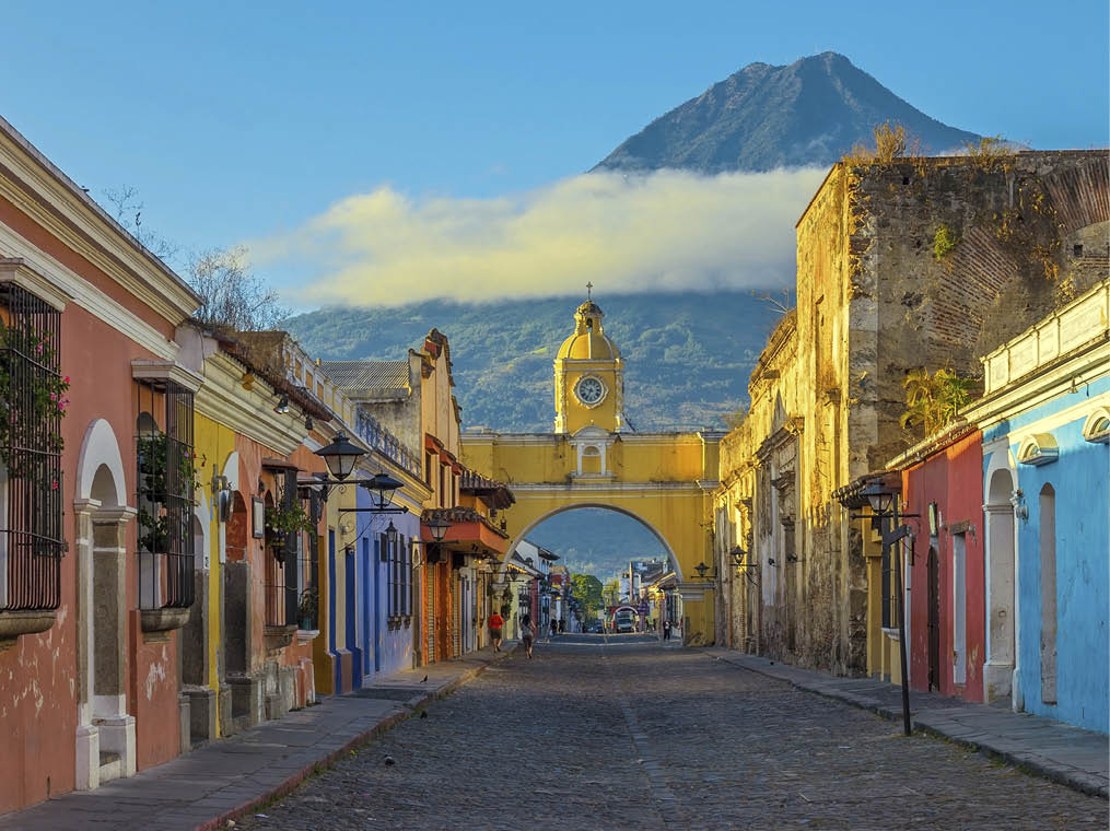 The historic city of Antigua at sunrise with a view over the main street and the Catalina arch and the Agua volcano in the background, Guatemala 