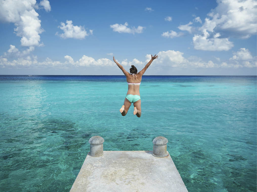 One woman jump in blue water from pier view from back on caribbean vacation