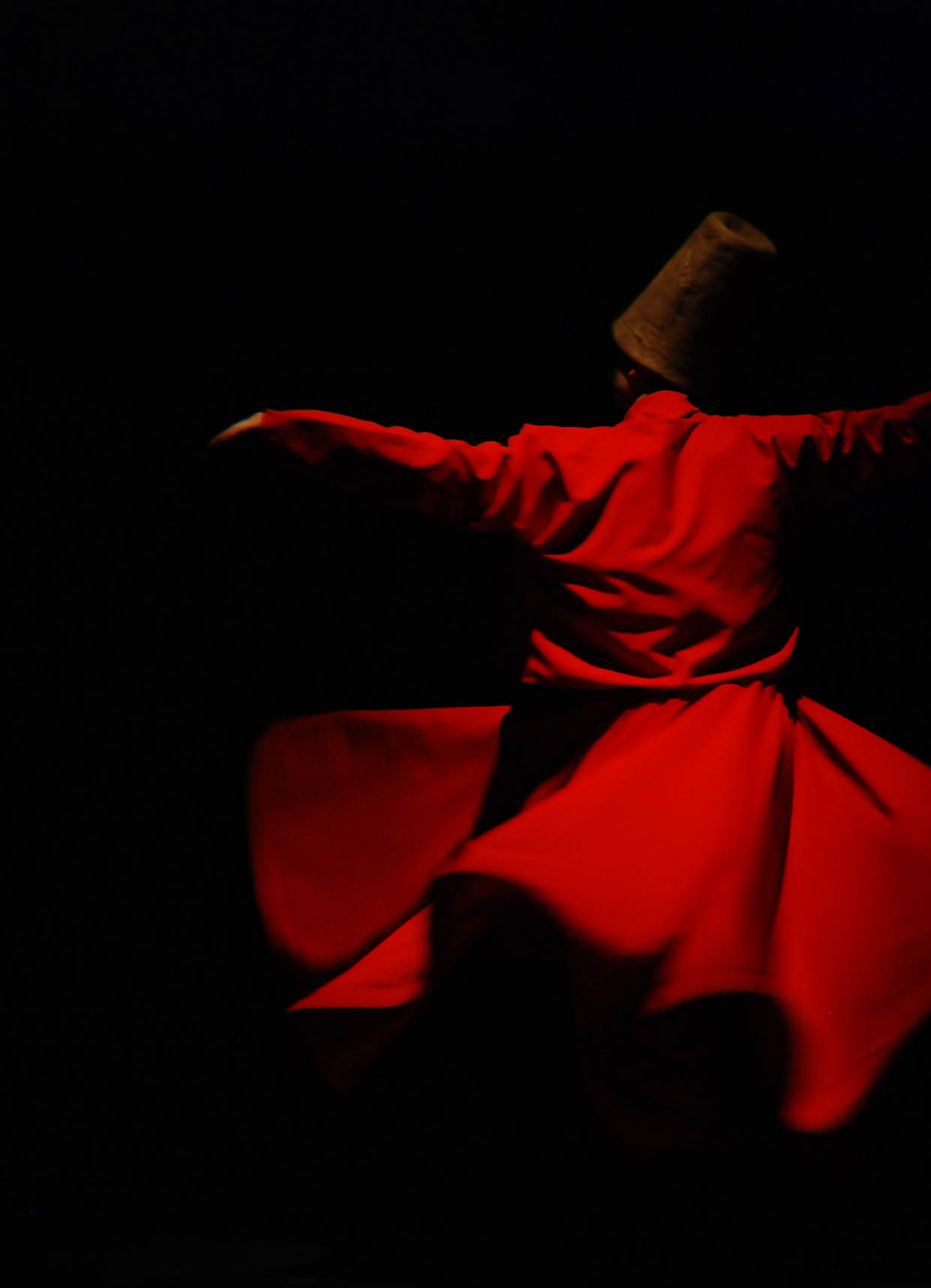 Whirling dervish in red garment on black background