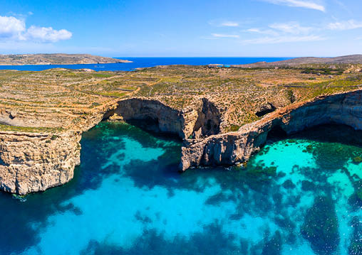 Malta  Comino island caves  Famous destination in Malta  Picturesque coastline of Comino island  Blue and crystal lagoons  Aerial view  From above  Sunny summer seascape 
