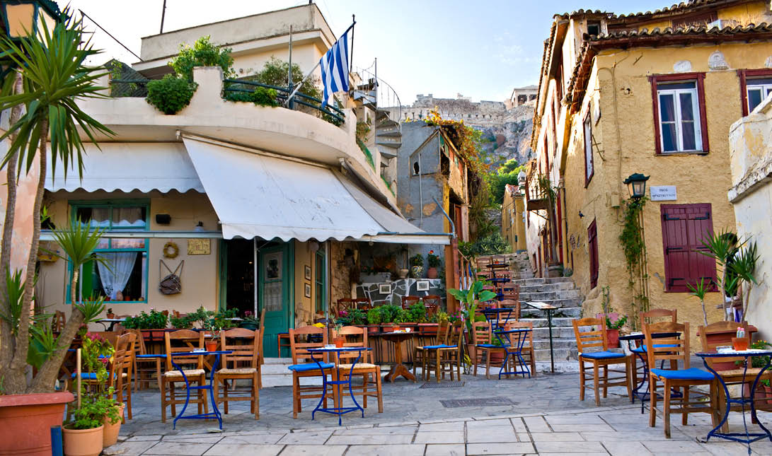 Athens, GREECE - OCTOBER 12, 2013: The old greek cafe surrounded by tiny tables in the yard, with a view on Acropolis on the top of the hill, on October 12 in Athens 