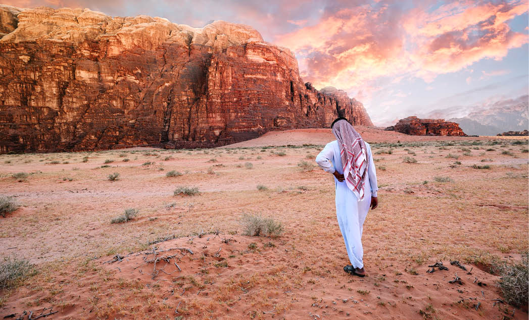 Arabian man in traditiona jordanian clothes (Keffiyeh - traditional Arabic headgear) walking in the wadi-rum desert at sunrise