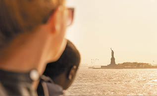 Tourists looking at Statue of Liberty silhouette in sunset from the staten island ferry, New York City, USA 