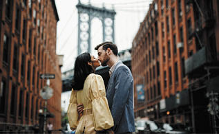 Love story in New York  Gorgeous couple of American man with beard and tender Eastern woman hug each other before the cityscape of Brooklyn bridge somewhere in New York