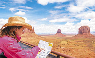 Woman wearing cowboy hat sitting and looking at map in Monument Valley with red rocks overview in Arizona USA