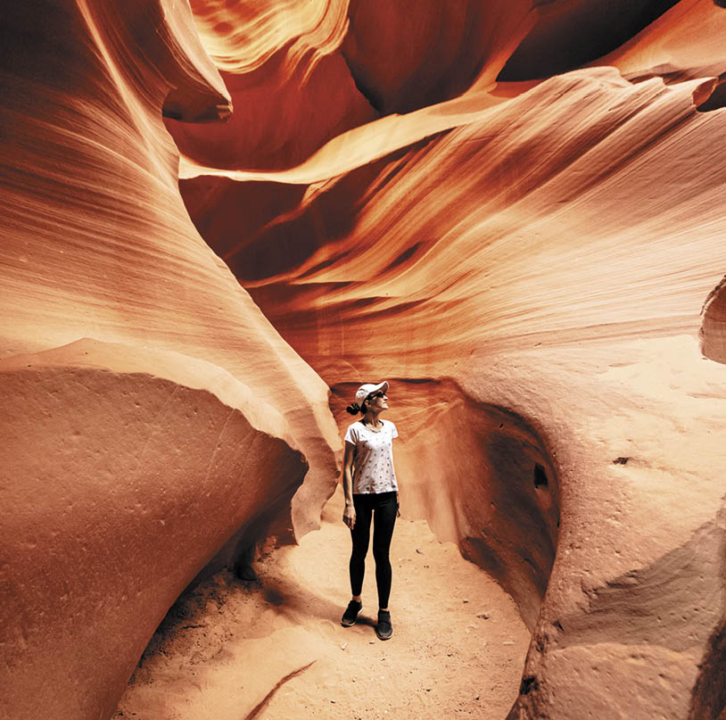 A young woman is walking on path between bizarre rocks in incredible Antelope Canyon, Arizona, USA 