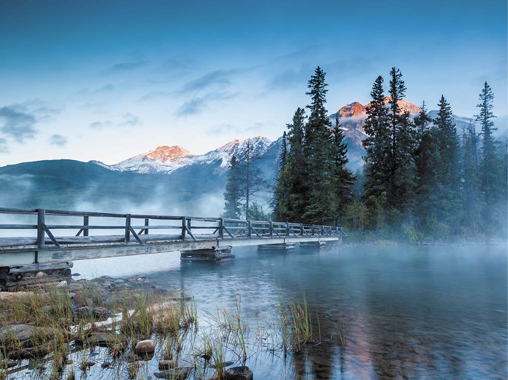First glimpse of a golden sunrise on a misty and foggy morning at Pyramid Lake in Jasper National Park, Alberta, Canada  The wooden bridge leads to Pyramid Island on the lake 