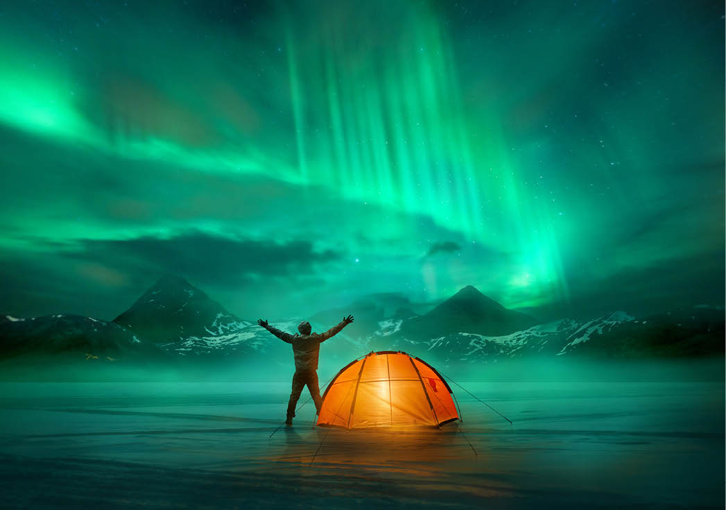 A man camping in wild northern mountains with an illuminated tent viewing a spectacular green northern lights aurora display  Photo composition 